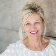 Attractive middle-aged blond woman with a beautiful smile standing against a receding wall looking directly at the camera