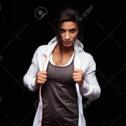 Young woman looking at camera with an attitude. Fitness female model in sportswear on black background